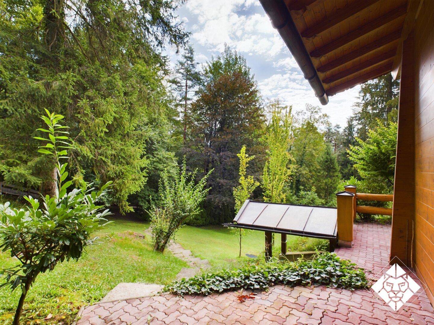 Kleiner gepflasterter Bereich mit Blick auf den grünen Garten und den umliegenden Wald.