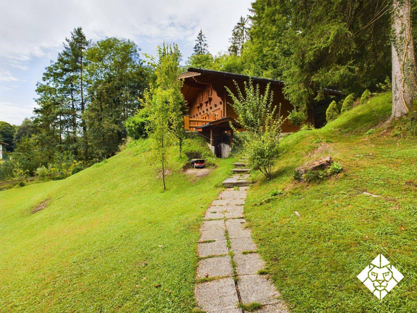 Steinweg führt durch den grünen Garten hinauf zum charmanten Holzhaus am Hang.