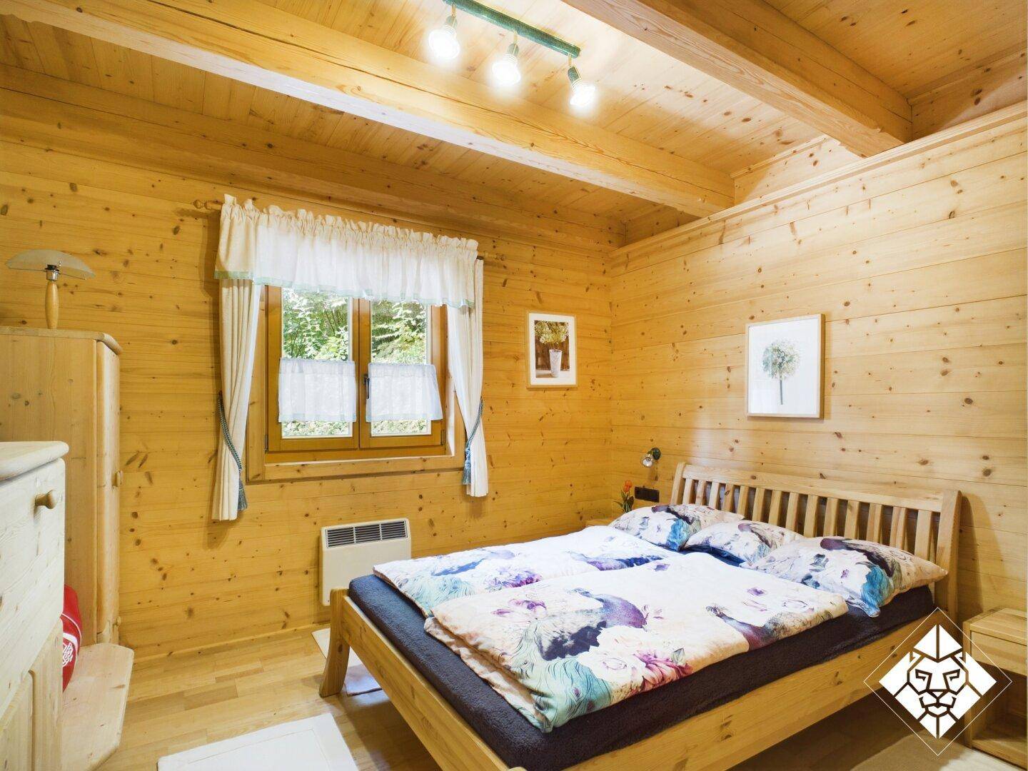 Gemütliches Schlafzimmer mit Holzvertäfelung, Holzboden und Blick ins Grüne durch das Fenster.