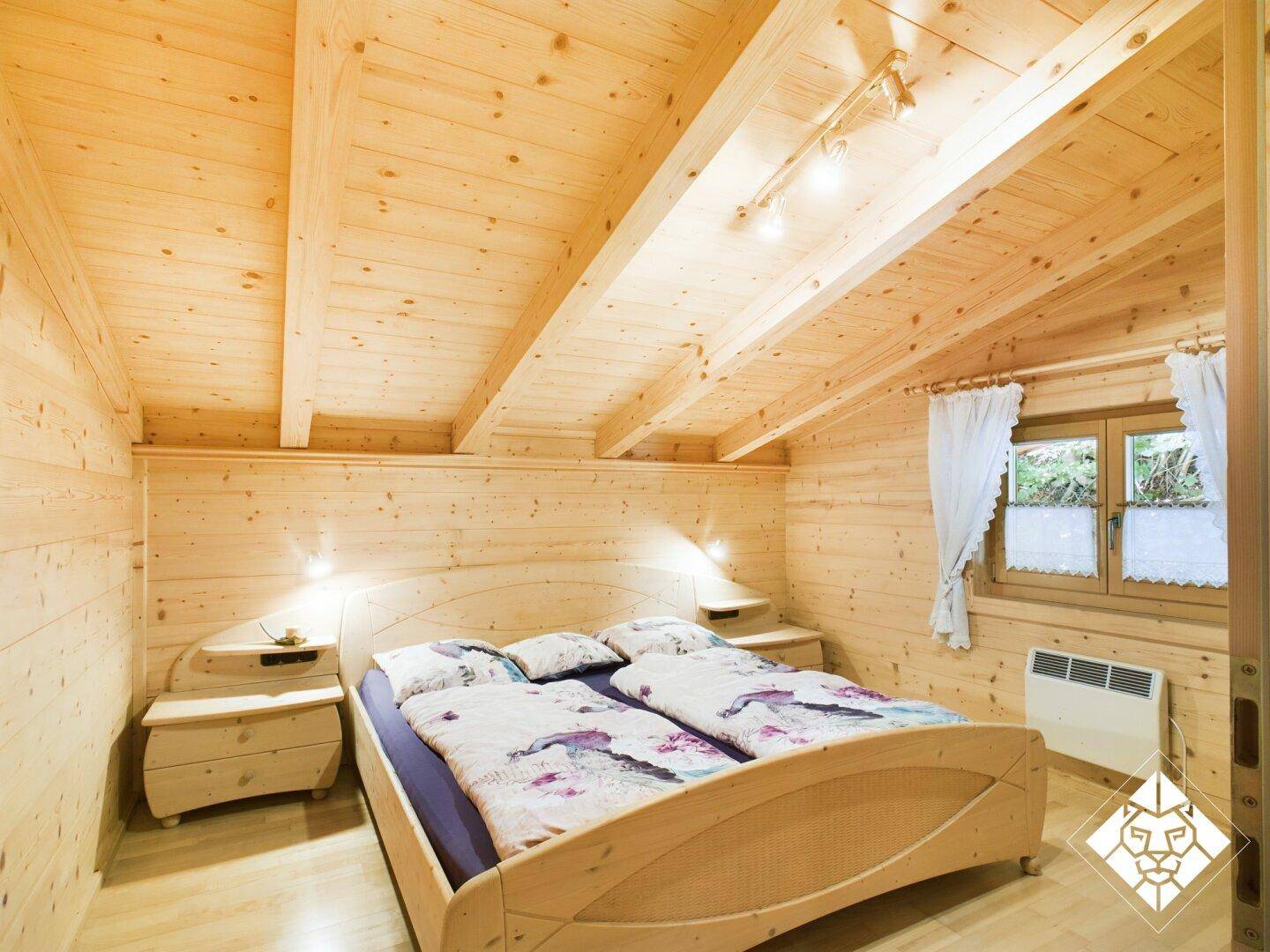 Gemütliches Schlafzimmer mit Doppelbett, Holzvertäfelung und Dachschrägen, hell durch das Fenster.