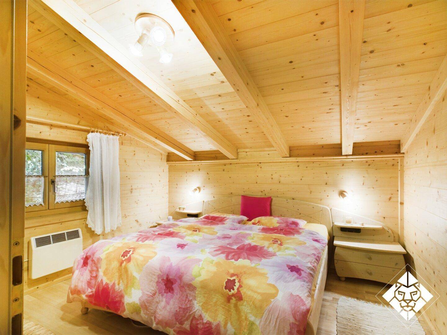 Helles Schlafzimmer mit Doppelbett, Holzvertäfelung und Dachschrägen, mit Blick ins Grüne.