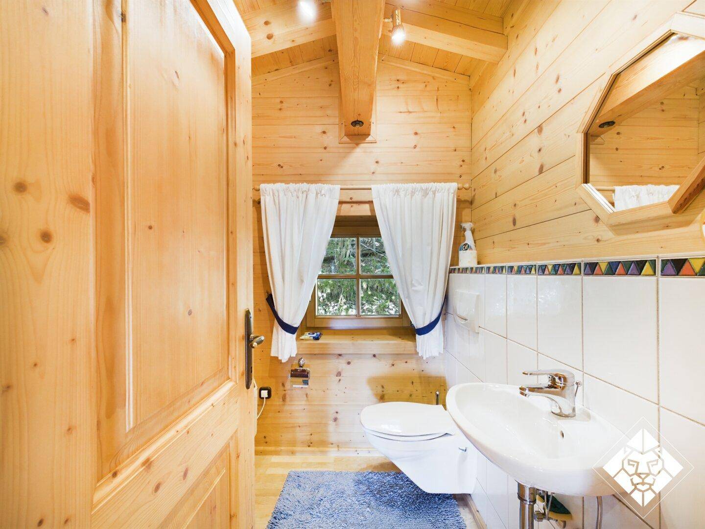 Kleines Badezimmer mit Holzvertäfelung, Fenster, Toilette und Waschbecken, hell und sauber.