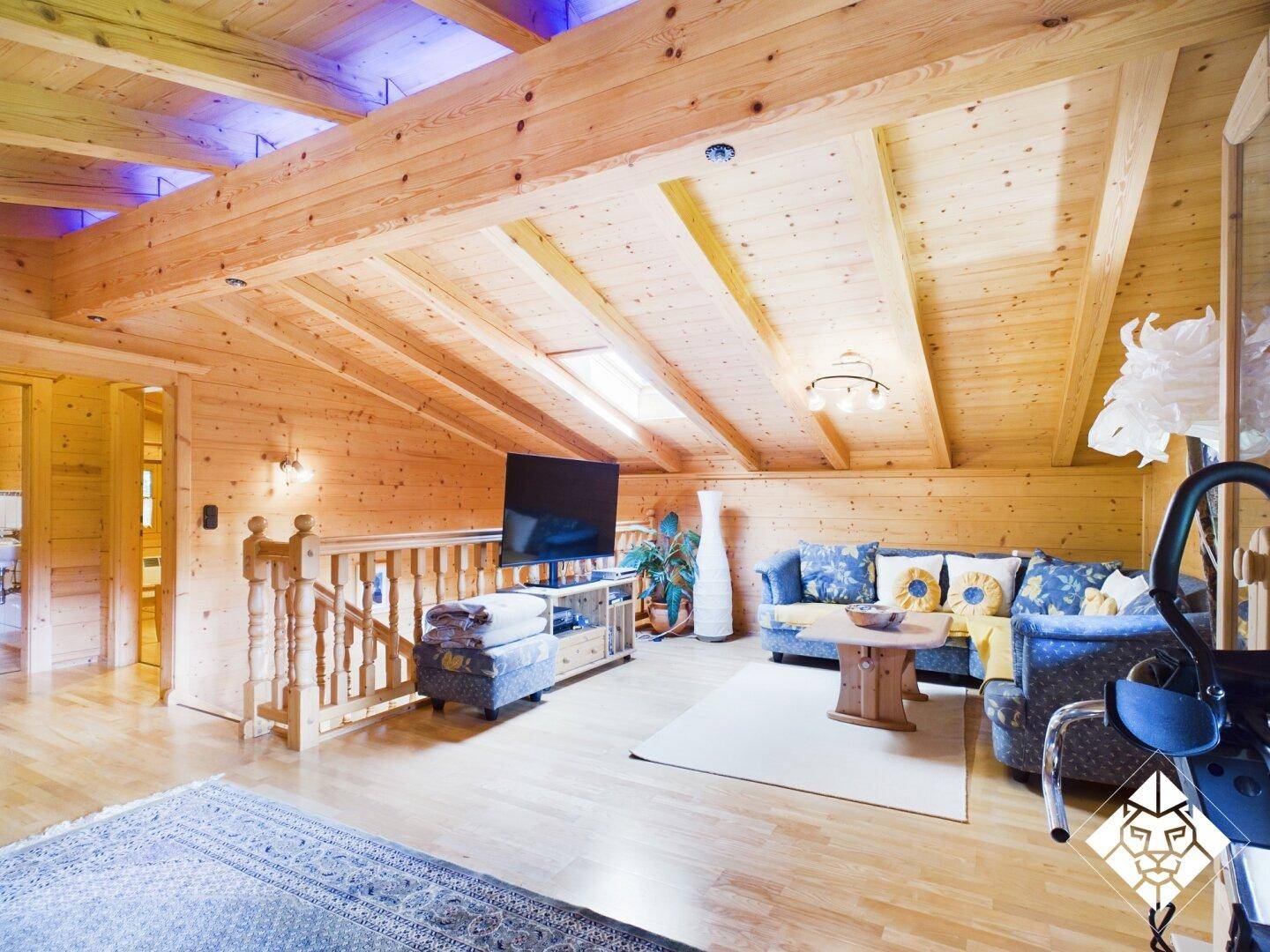 Offener Wohnbereich im Dachgeschoss mit Holzbalken, gemütlicher Sitzecke und Blick auf die Galerie.