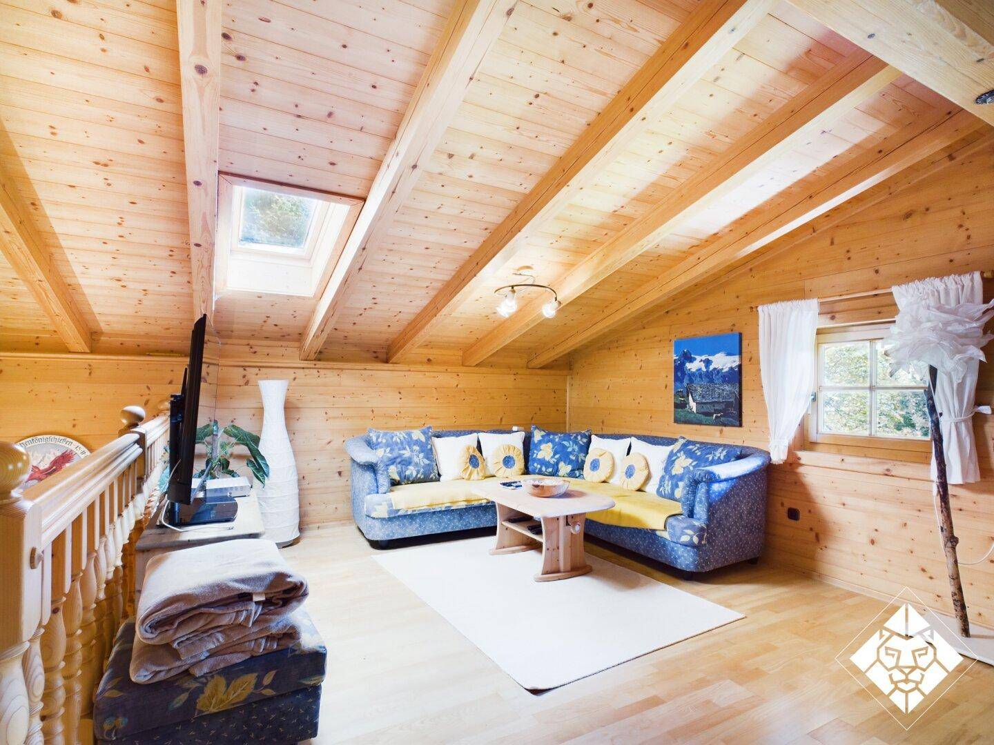 Geräumiger Wohnbereich im Dachgeschoss mit gemütlichem Ecksofa, Fernseher und Dachfenster.