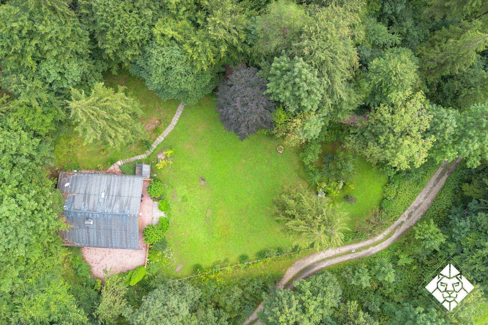 Luftaufnahme eines Hauses mit großem Rasen und umgebendem Waldgebiet in ländlicher Umgebung.