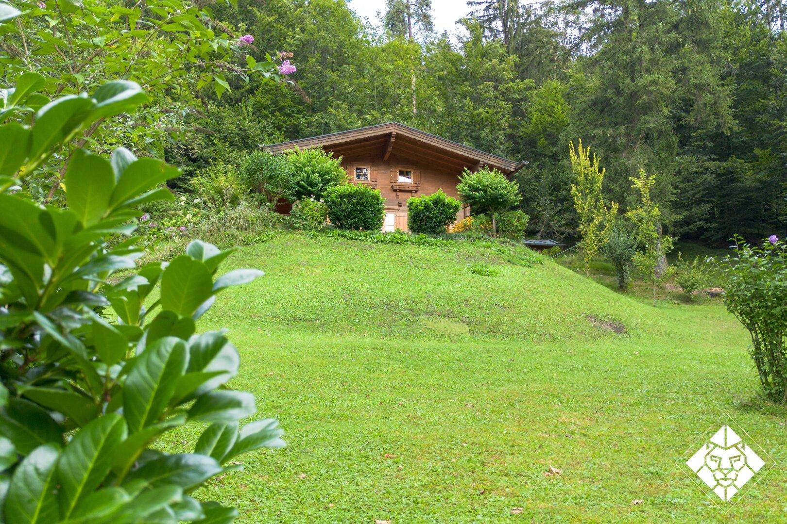Idyllisches Holzhaus auf einem Hügel, umgeben von einem weitläufigen grünen Garten und Wald.