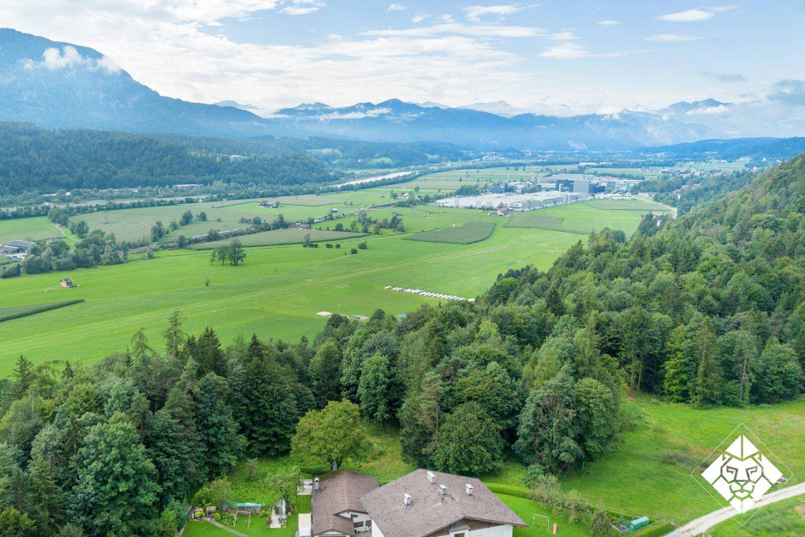 Weitläufige Luftaufnahme einer ländlichen Landschaft mit grünen Feldern, Wäldern und Bergen im Hintergrund.