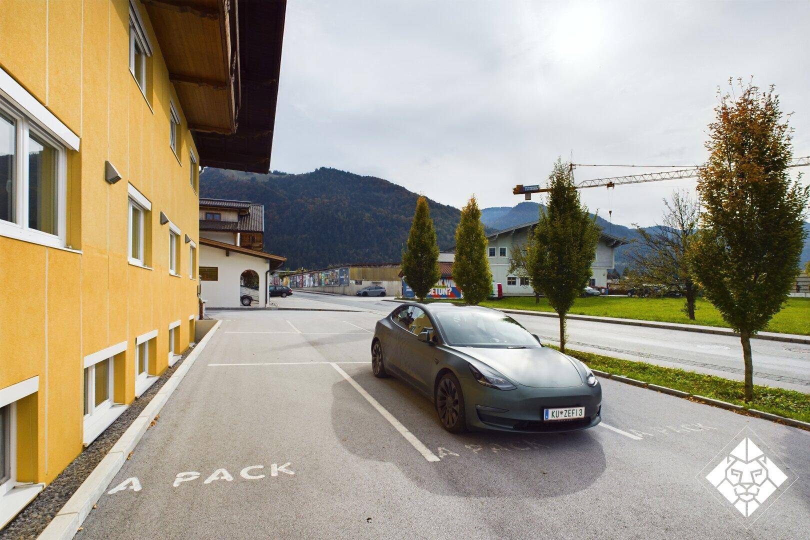 Außenansicht des Gebäudes mit Parkplätzen, einem geparkten Auto und Bergblick im Hintergrund.