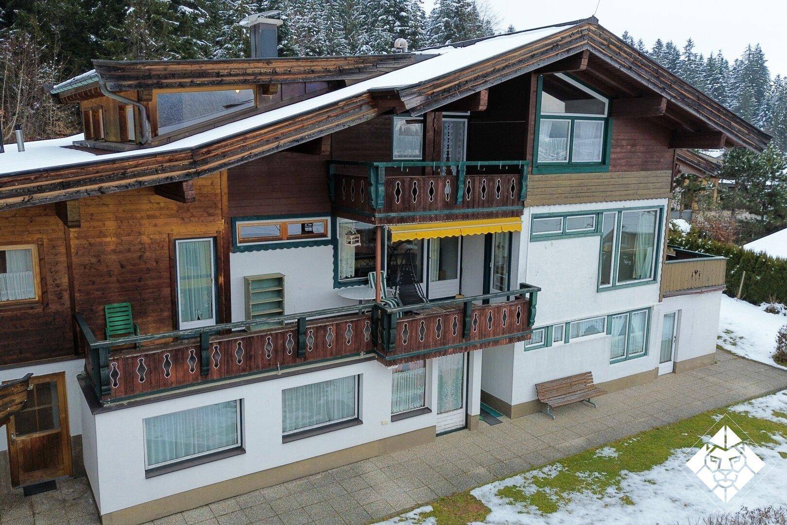 Traditionelles Holzhaus im alpinen Stil mit Balkonen und verschneiter Umgebung am Waldrand.