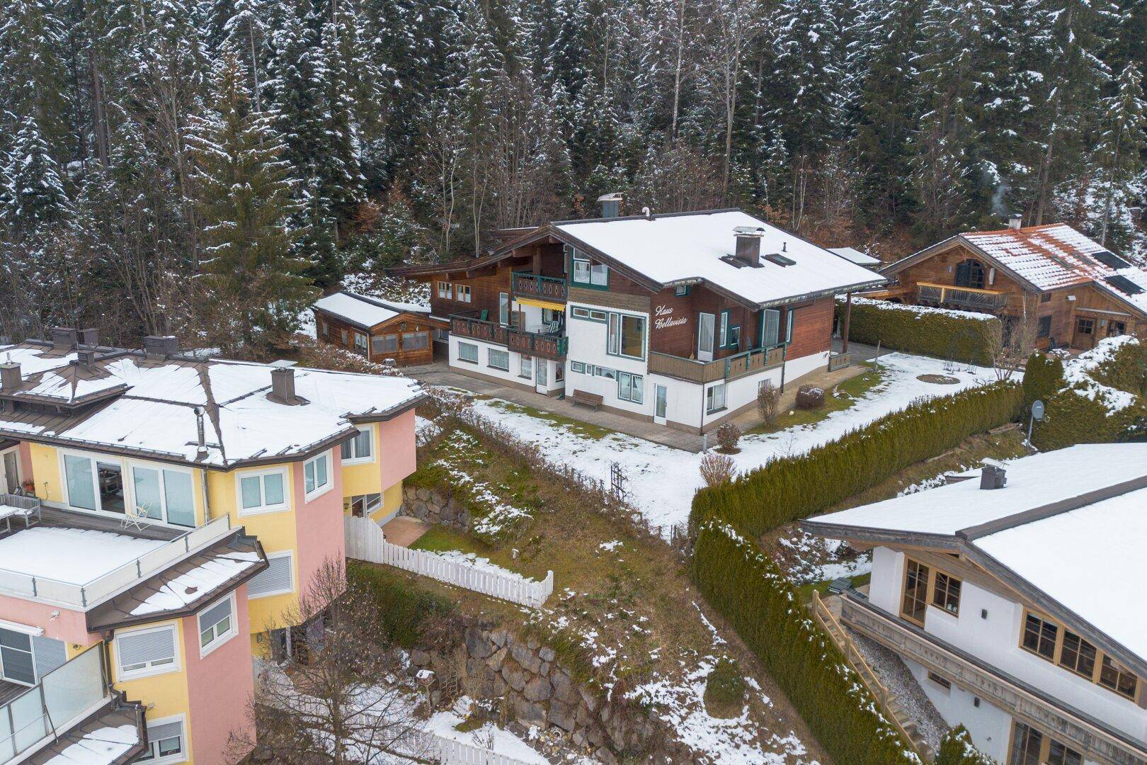 Luftaufnahme des traditionellen Holzhauses in verschneiter Berglandschaft mit umliegenden Gebäuden.