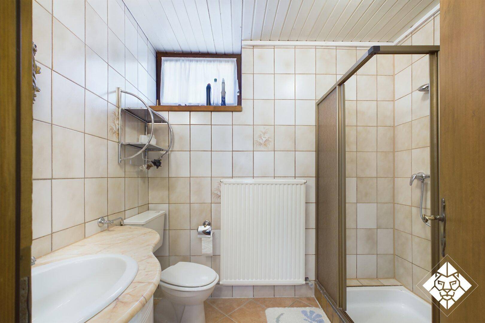 Traditionelles Badezimmer mit Duschkabine, Waschbecken, WC und Fenster.