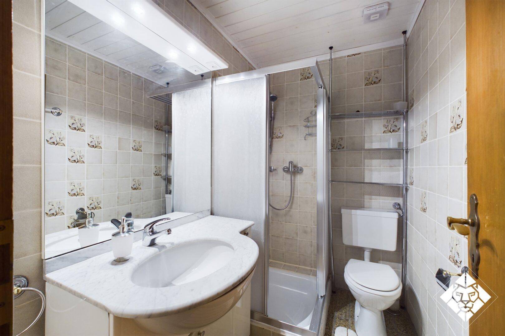Badezimmer mit Duschkabine, Waschbecken und WC, gefliest in hellen Mustern.