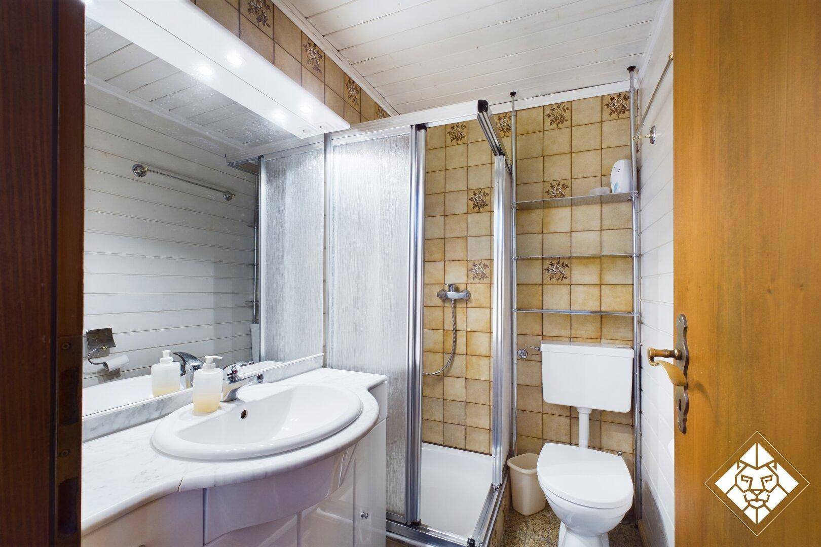 Badezimmer mit Duschkabine, Waschbecken und WC, gefliest in warmen Farbtönen.