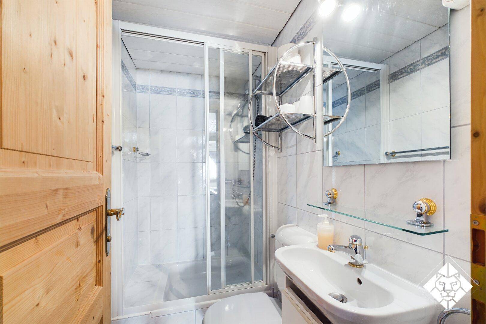 Badezimmer mit Duschkabine, Waschbecken und WC, gefliest in hellen Tönen.