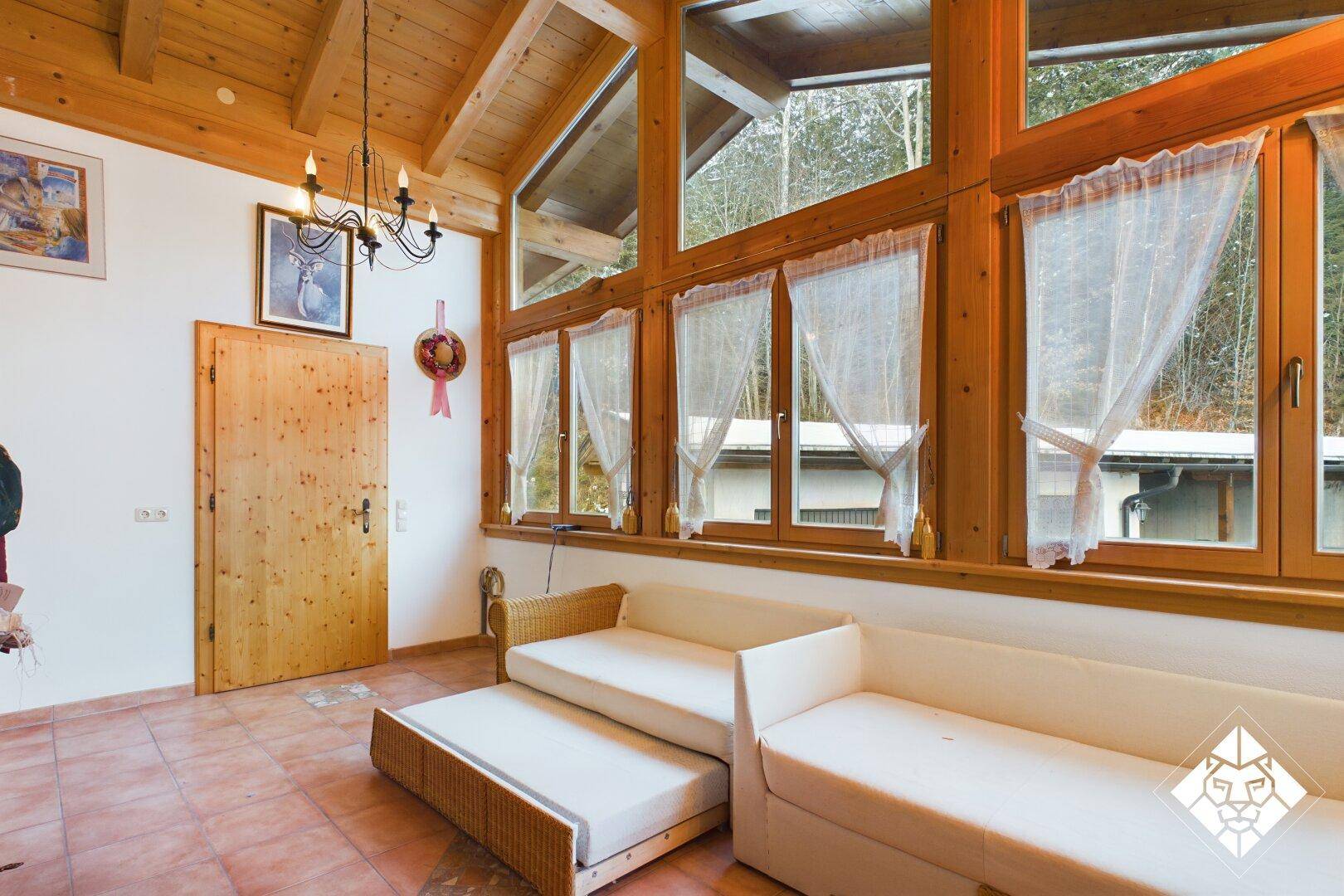 Heller Wohnbereich mit hohen Fenstern, Holzbalkendecke und Terracottaboden.