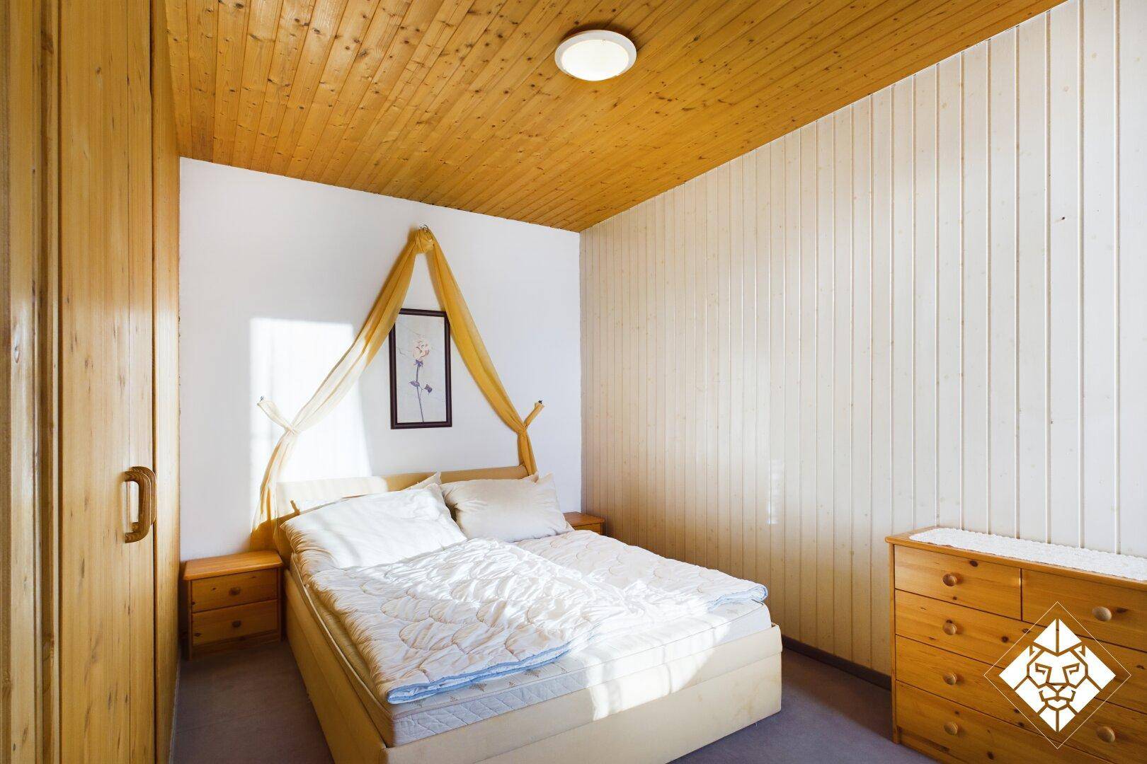 Helles Schlafzimmer mit Holzmöbeln, Doppelbett und holzgetäfelter Decke.