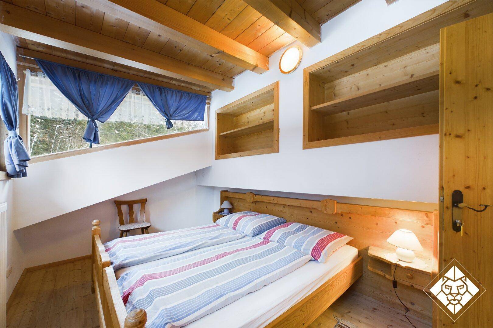 Rustikales Schlafzimmer mit Holzbalkendecke, Doppelbett und schrägen Wänden.