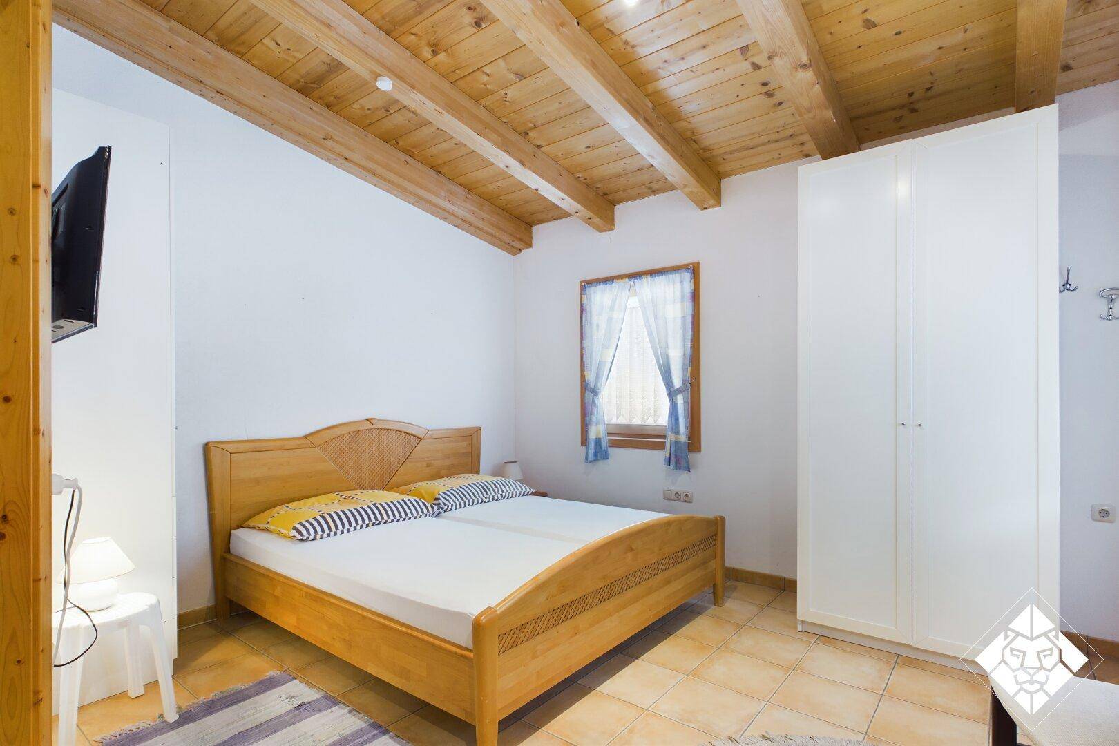 Helles Schlafzimmer mit Holzbett, weißem Kleiderschrank und Holzbalkendecke.