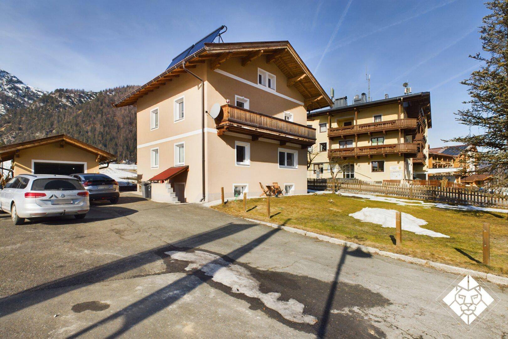 Haus mit Balkon und Garage, umgeben von winterlicher Landschaft und Bergen.
