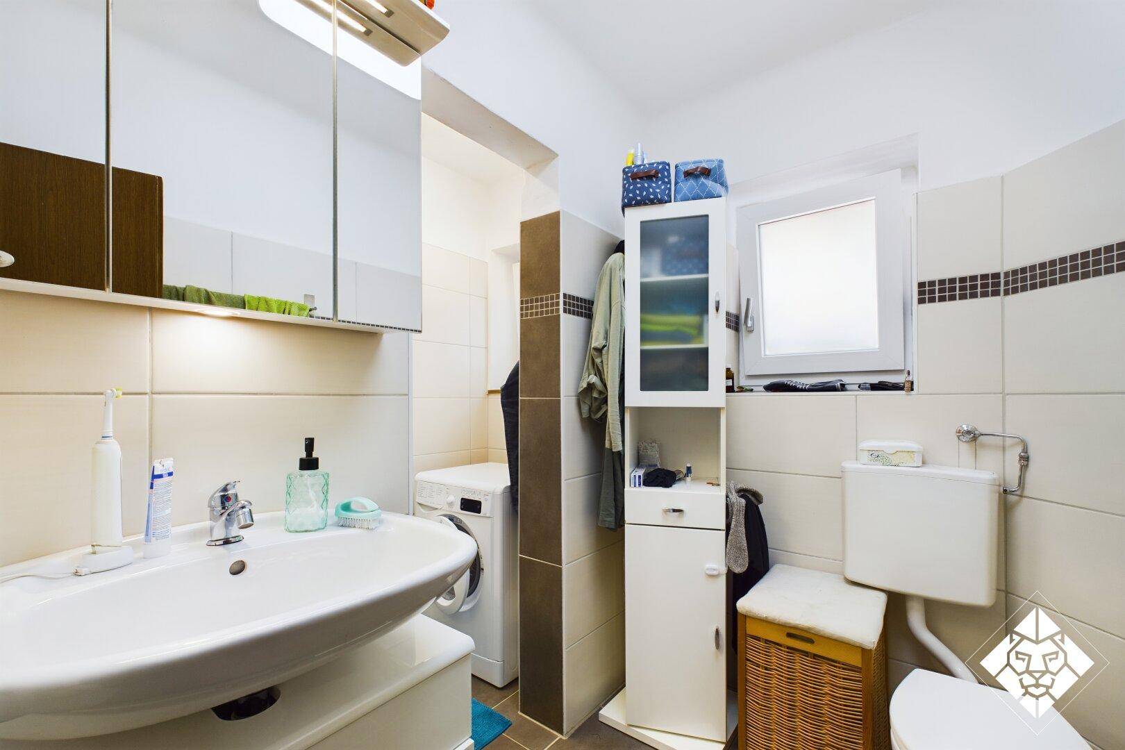 Funktionales Badezimmer mit Waschbecken, Toilette und Fenster für Tageslicht.