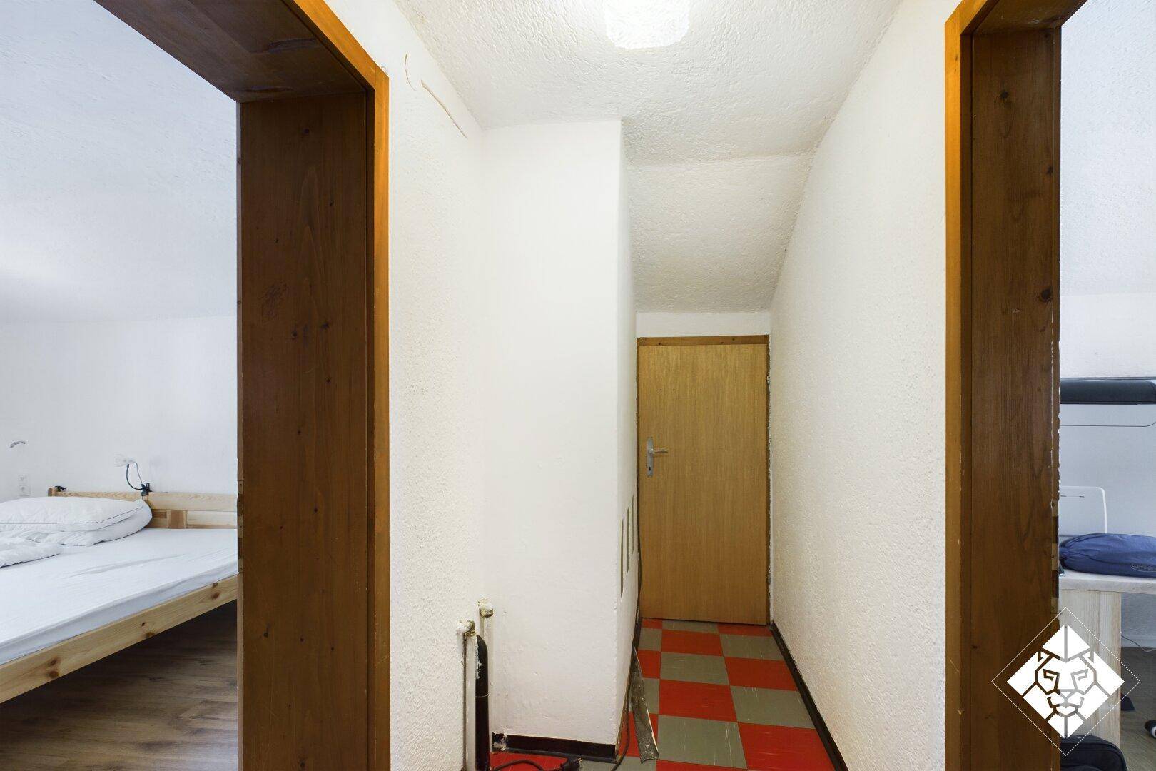 Schmaler Flur mit Holztür und kariertem Boden, der zu einem Schlafzimmer führt.