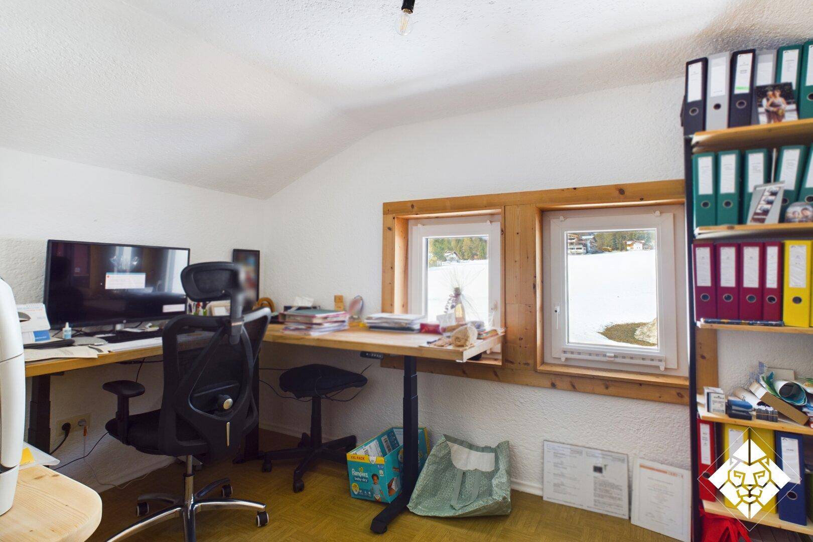 Helles Büro mit Schreibtisch, Regalen und Fenstern mit Blick auf die verschneite Landschaft.