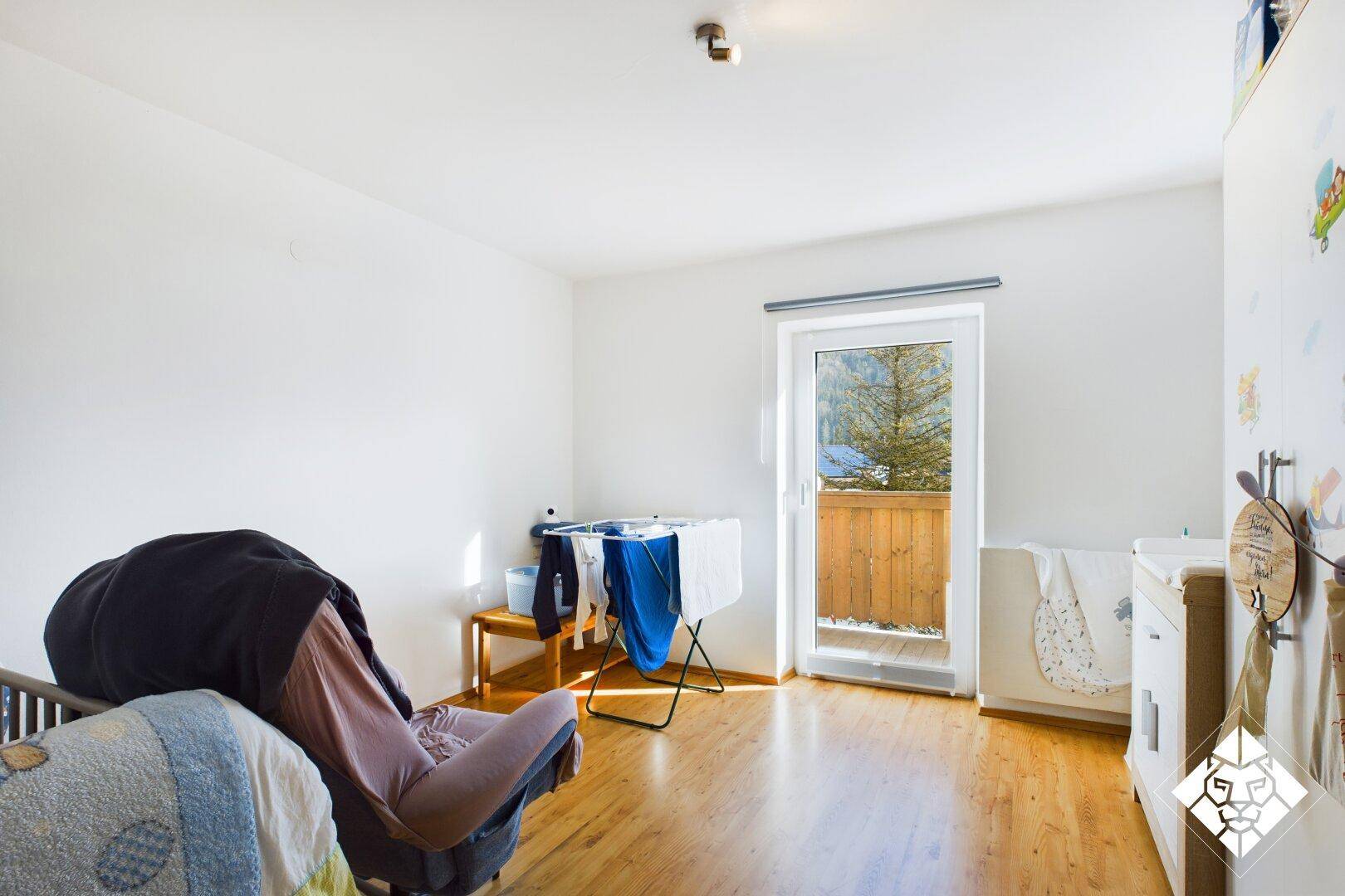 Helles Kinderzimmer mit Holzboden, Balkonzugang und Blick auf die verschneite Landschaft.