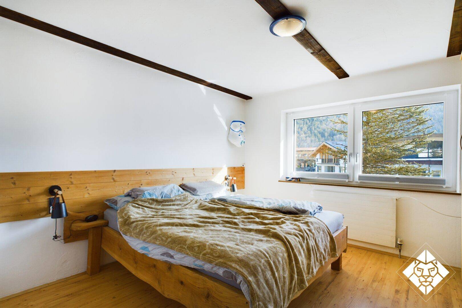 Gemütliches Schlafzimmer mit Holzbett, Parkettboden und Blick auf die umliegende Natur.