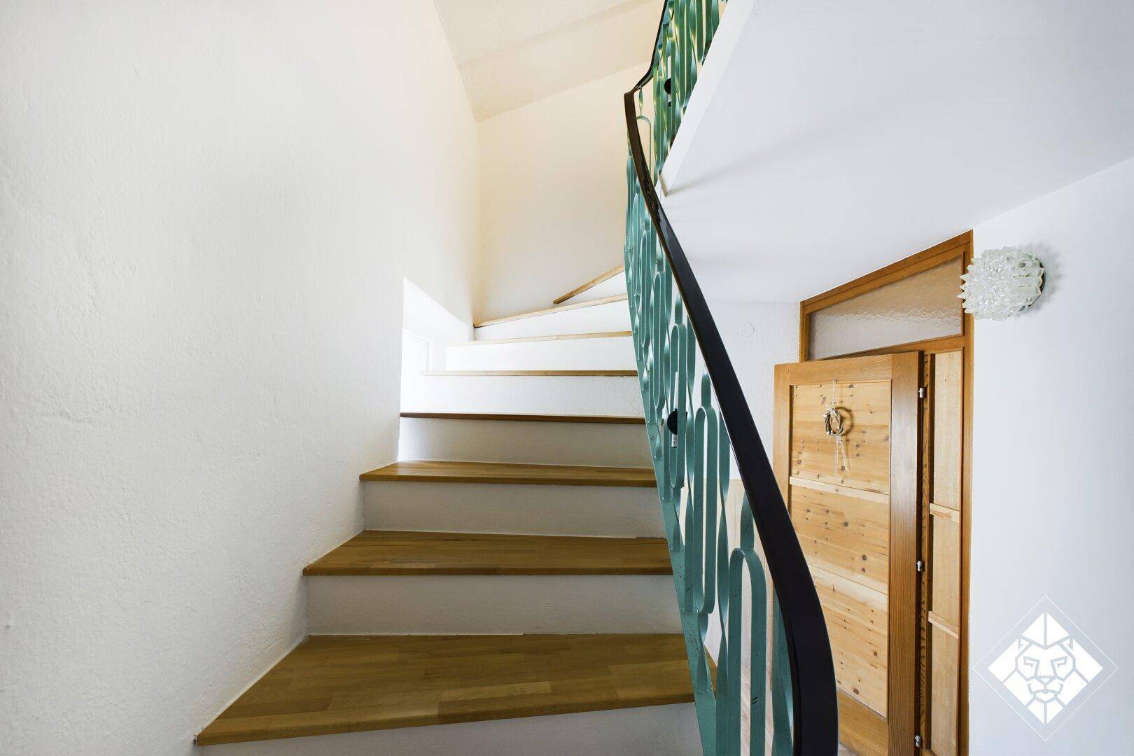 Treppenhaus mit Holzstufen und grünem Geländer, das die Stockwerke verbindet.
