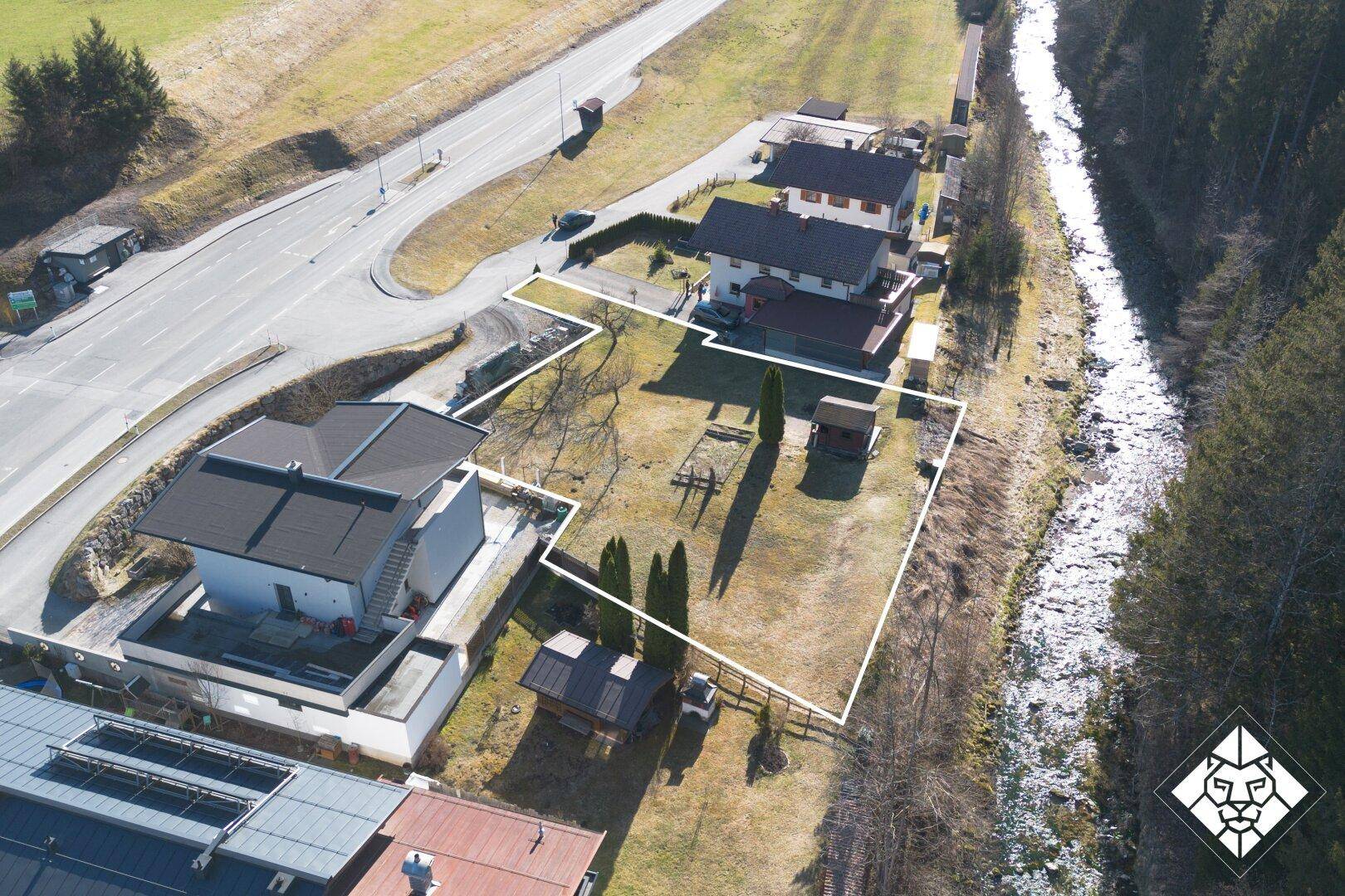 Luftaufnahme des Grundstücks mit Flusslauf, angrenzender Straße und bewaldeter Umgebung.