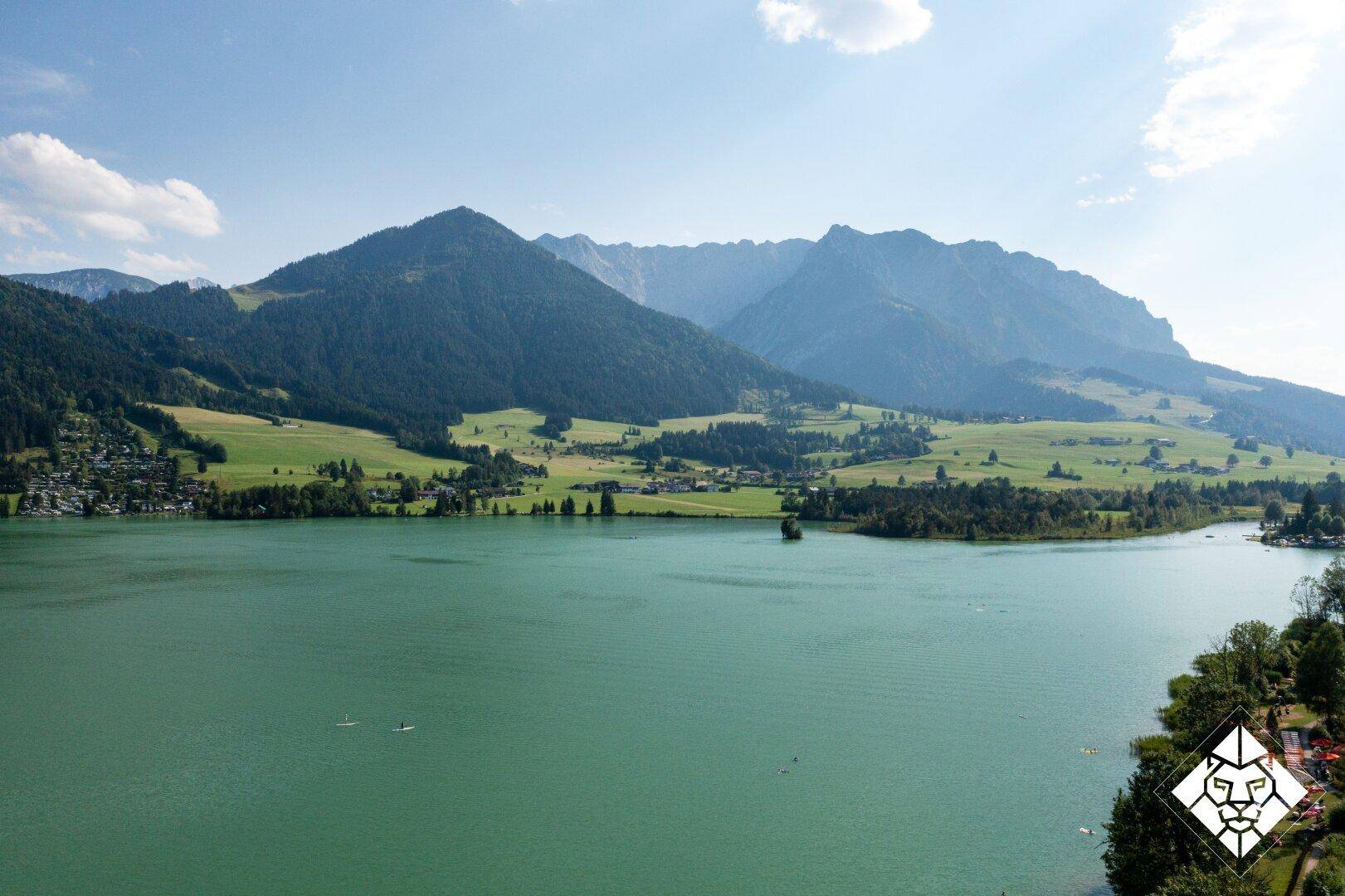 Weitläufiger Blick auf einen großen See mit imposanten Bergen und grünen Tälern in der Ferne.