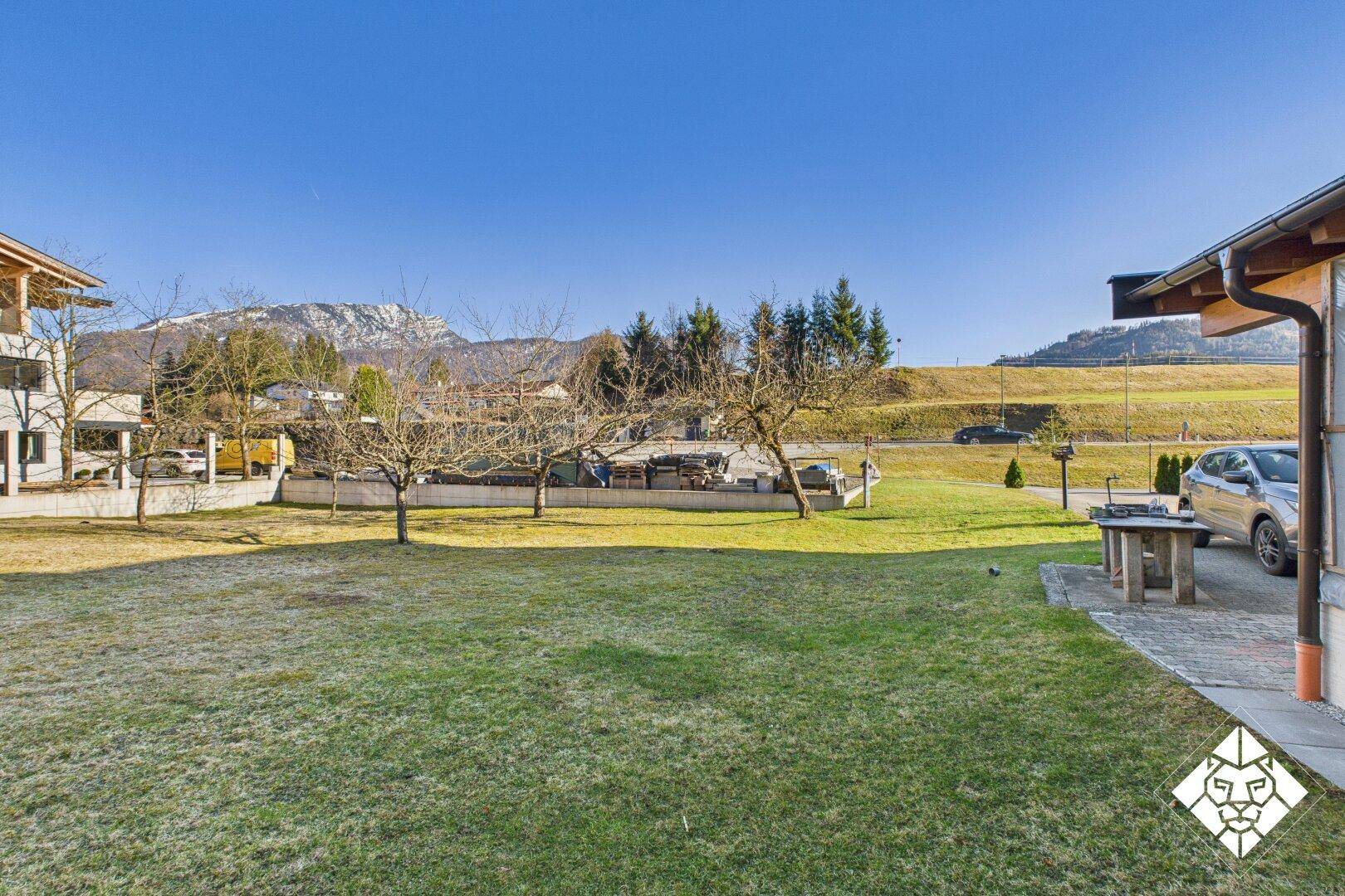 Großer Garten mit Rasenfläche, angrenzendem Parkplatz und Blick auf die umliegende Berglandschaft.