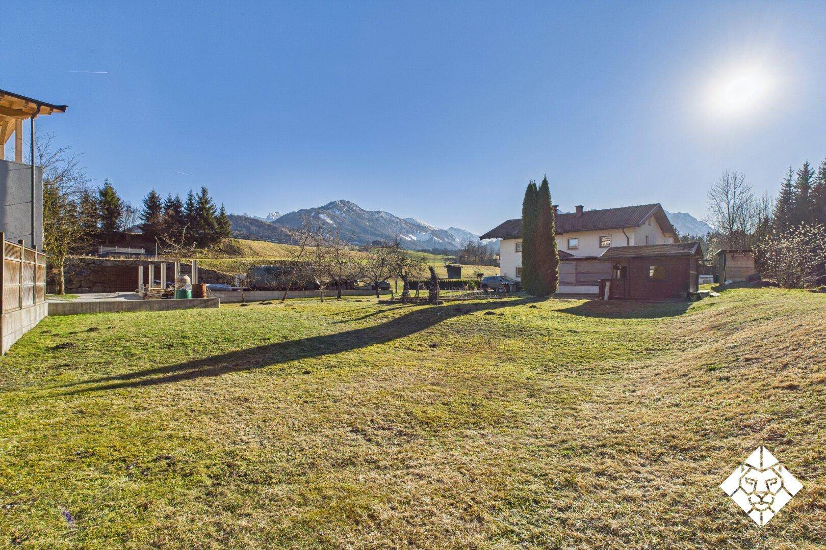Weitläufiger Gartenbereich mit grüner Rasenfläche und malerischem Bergblick unter strahlendem Sonnenschein.