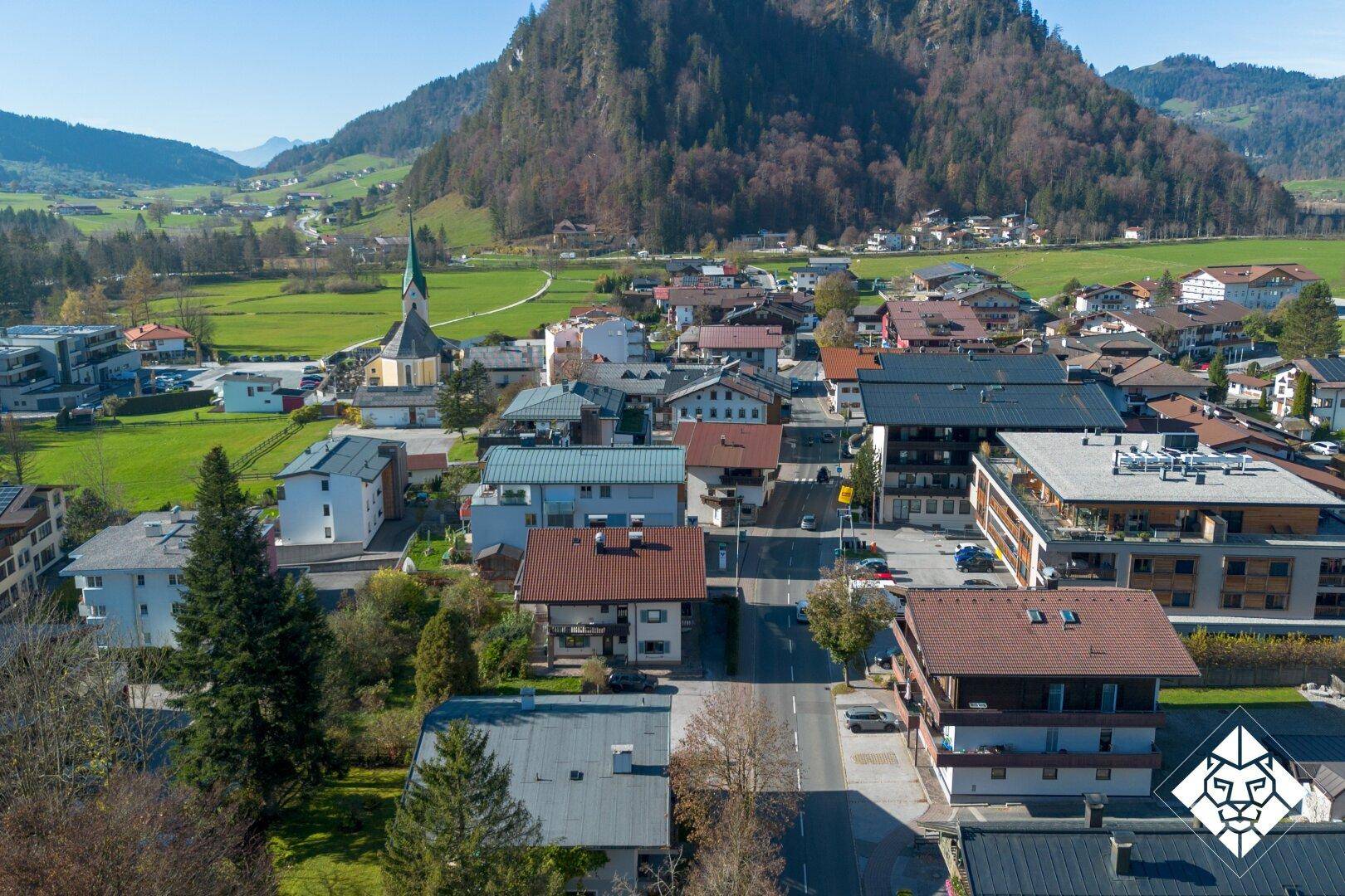 Weitläufige Luftaufnahme einer charmanten Stadt mit Kirche, eingebettet in eine grüne Berglandschaft.