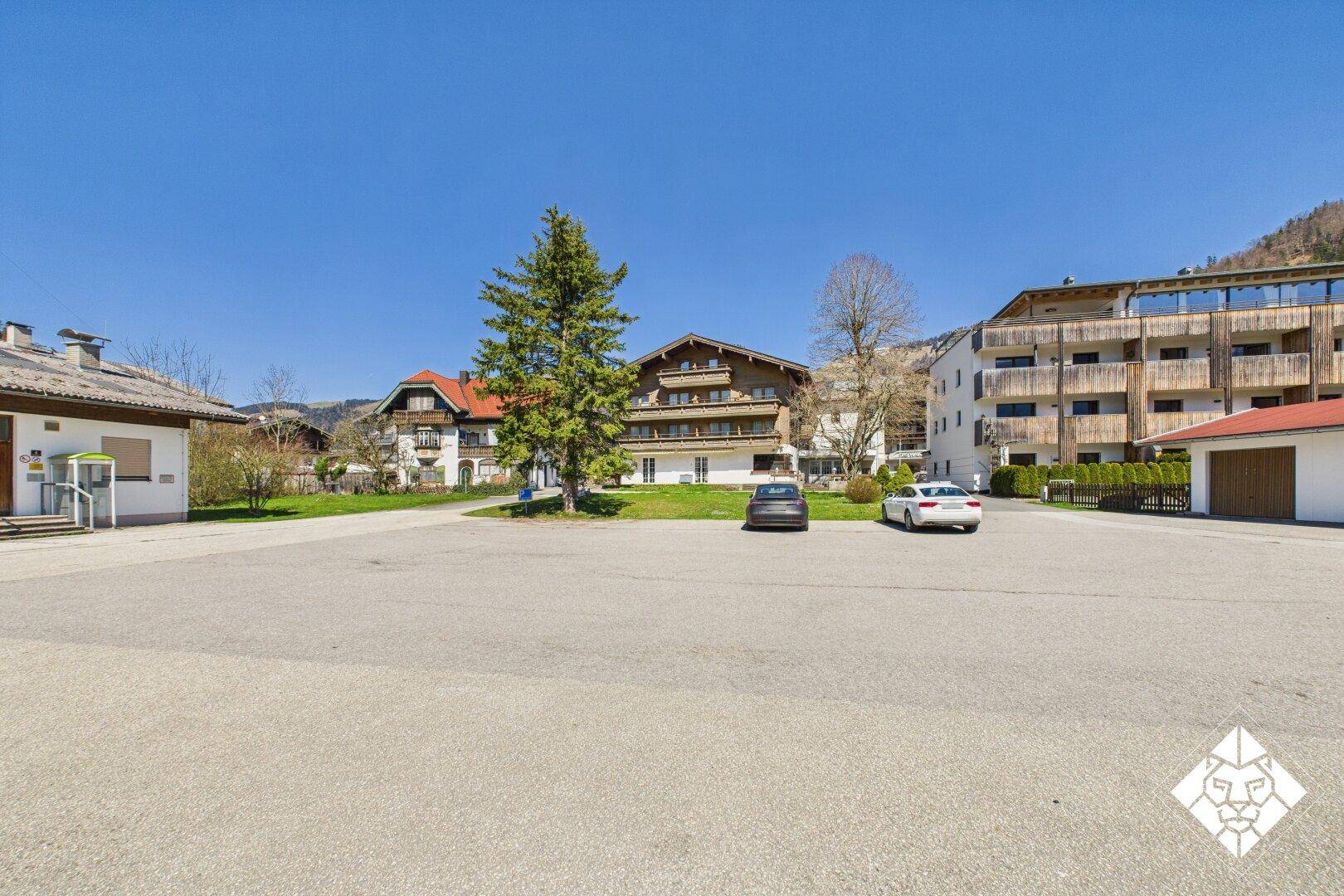 Großer Außenparkplatz mit Gebäuden und Bergen im Hintergrund unter strahlend blauem Himmel.