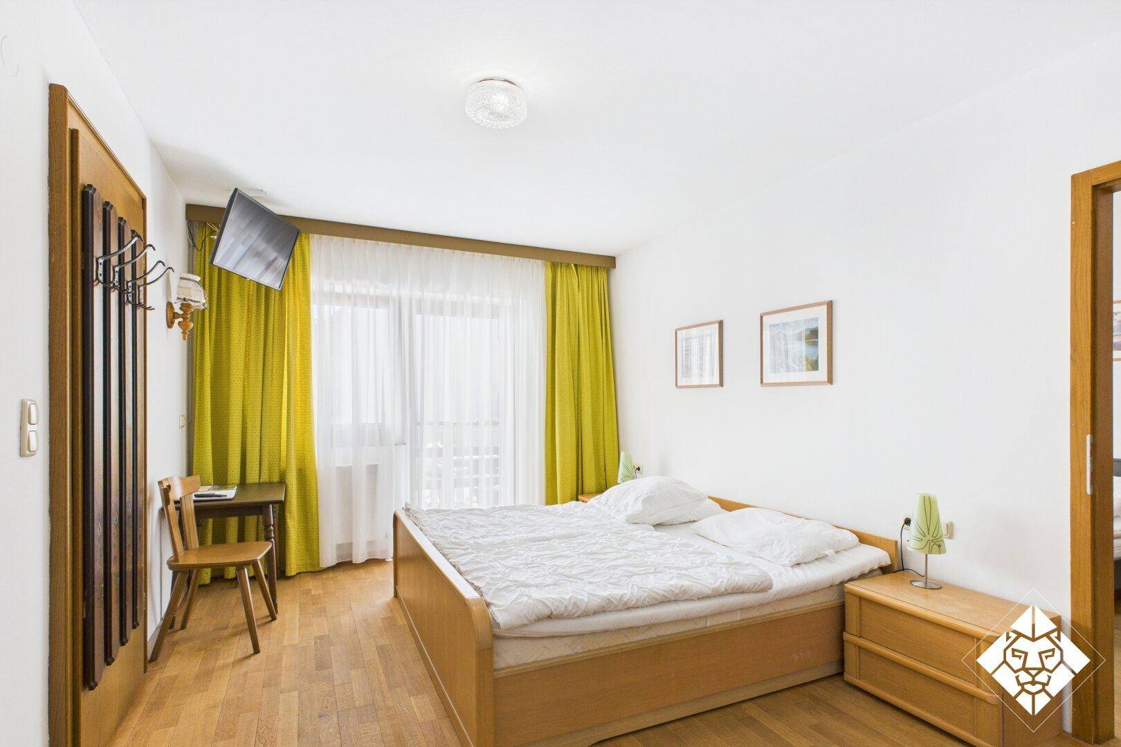 Schlafzimmer mit Doppelbett, Holzmöbeln und leuchtend gelben Vorhängen, hell und freundlich.
