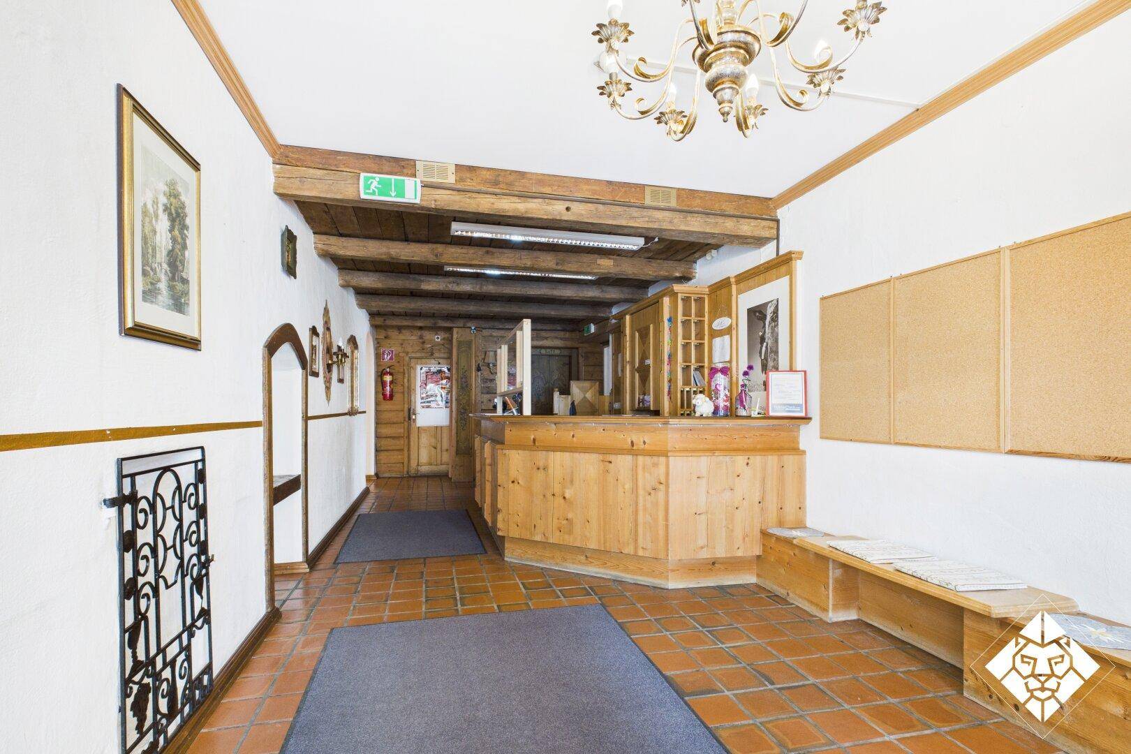 Empfangsbereich mit rustikalem Holztresen, sichtbaren Deckenbalken und Terrakottafliesenboden.