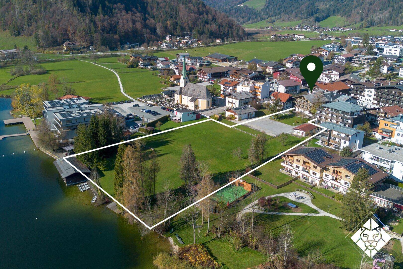Luftaufnahme einer Stadt am See mit markiertem Grundstück und Tennisplatz, umgeben von Bergen.