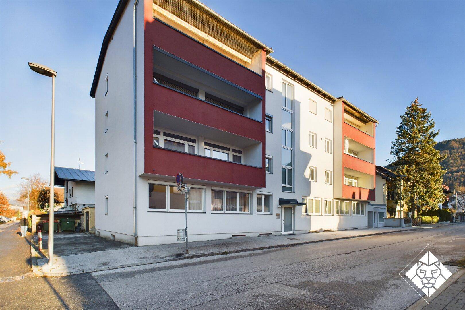 Mehrstöckiges Wohngebäude mit weißer und roter Fassade, Balkonen und großen Fenstern.