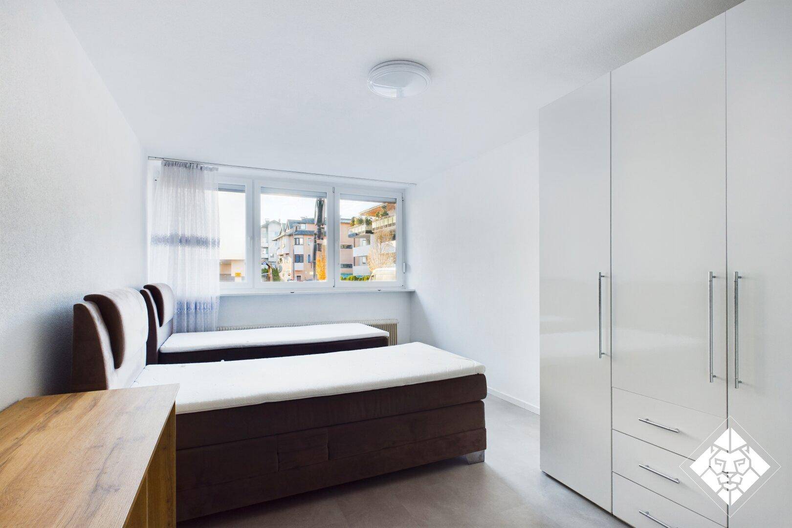 Schlafzimmer mit zwei Einzelbetten, weißem Kleiderschrank und Blick auf die Umgebung.