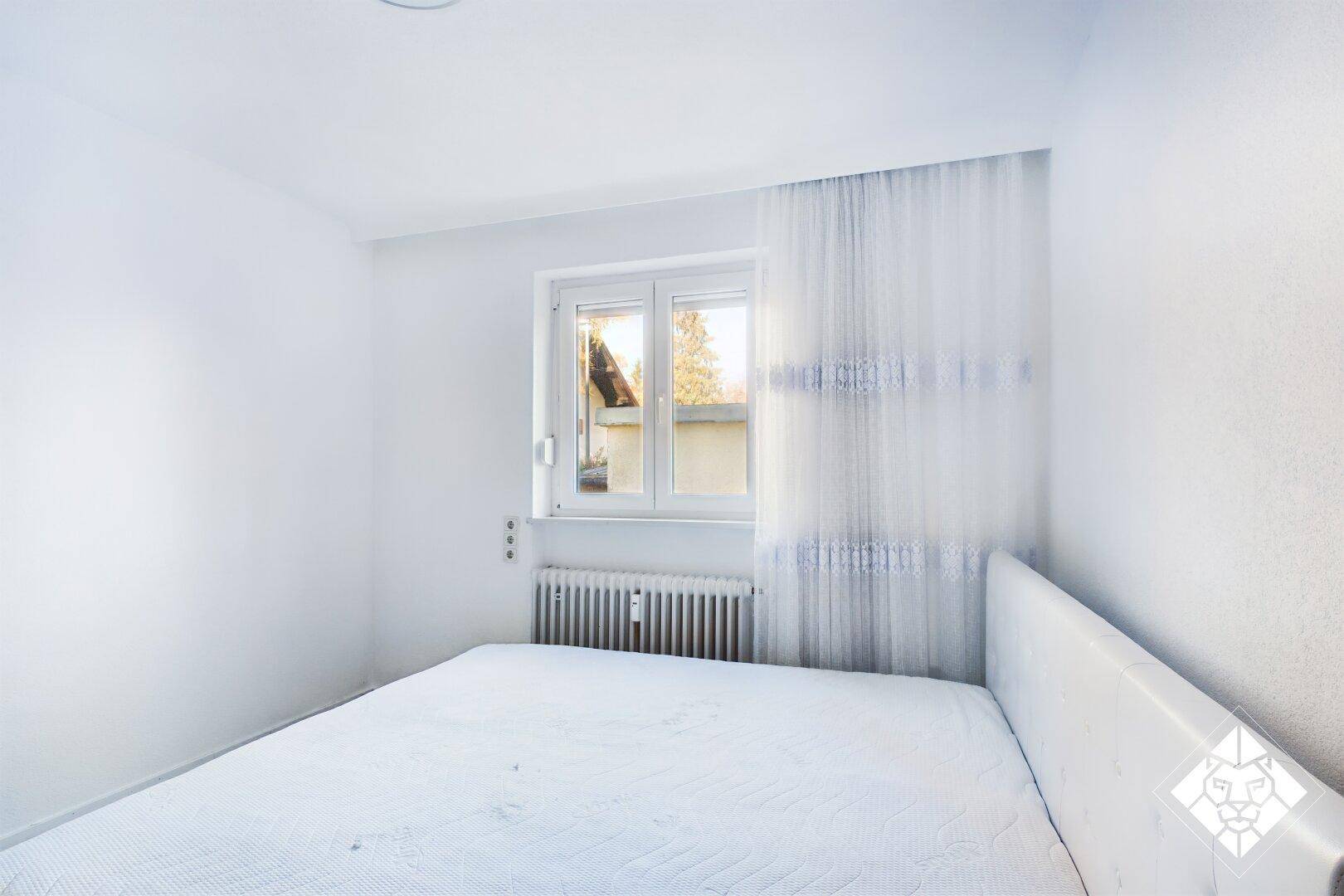 Helles Schlafzimmer mit einem Einzelbett und einem Fenster, das Tageslicht hereinlässt.