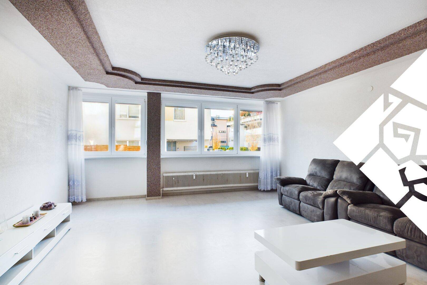 Geräumiges Wohnzimmer mit großem Fenster, dunklem Sofa und dekorativer Deckenleiste.