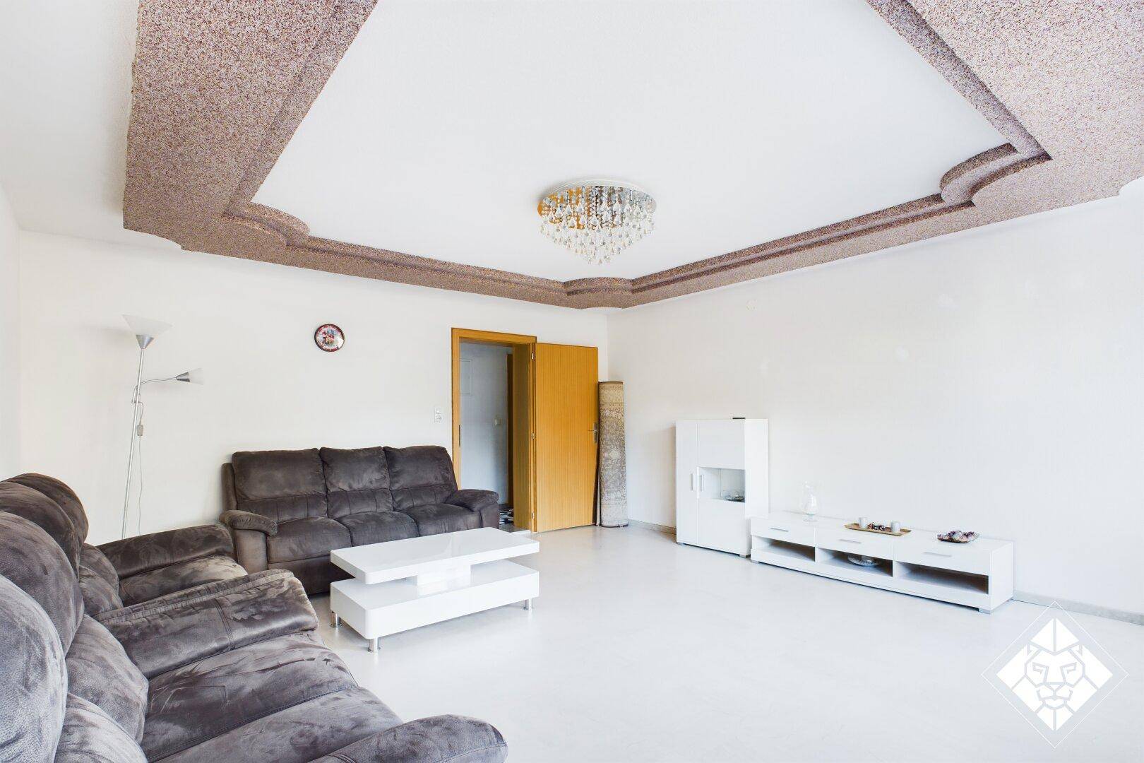 Wohnzimmer mit bequemer Couch, weißem Couchtisch und dekorativer Decke, die zum Flur führt.