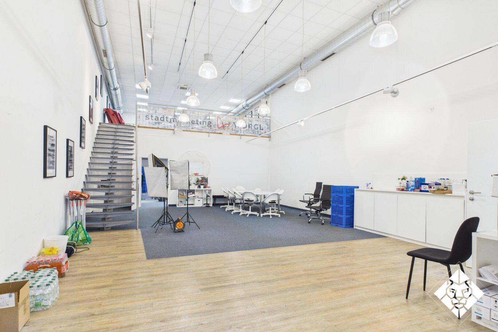 Großer Bürobereich mit Teppichboden, Treppe zum Obergeschoss und Besprechungstisch.