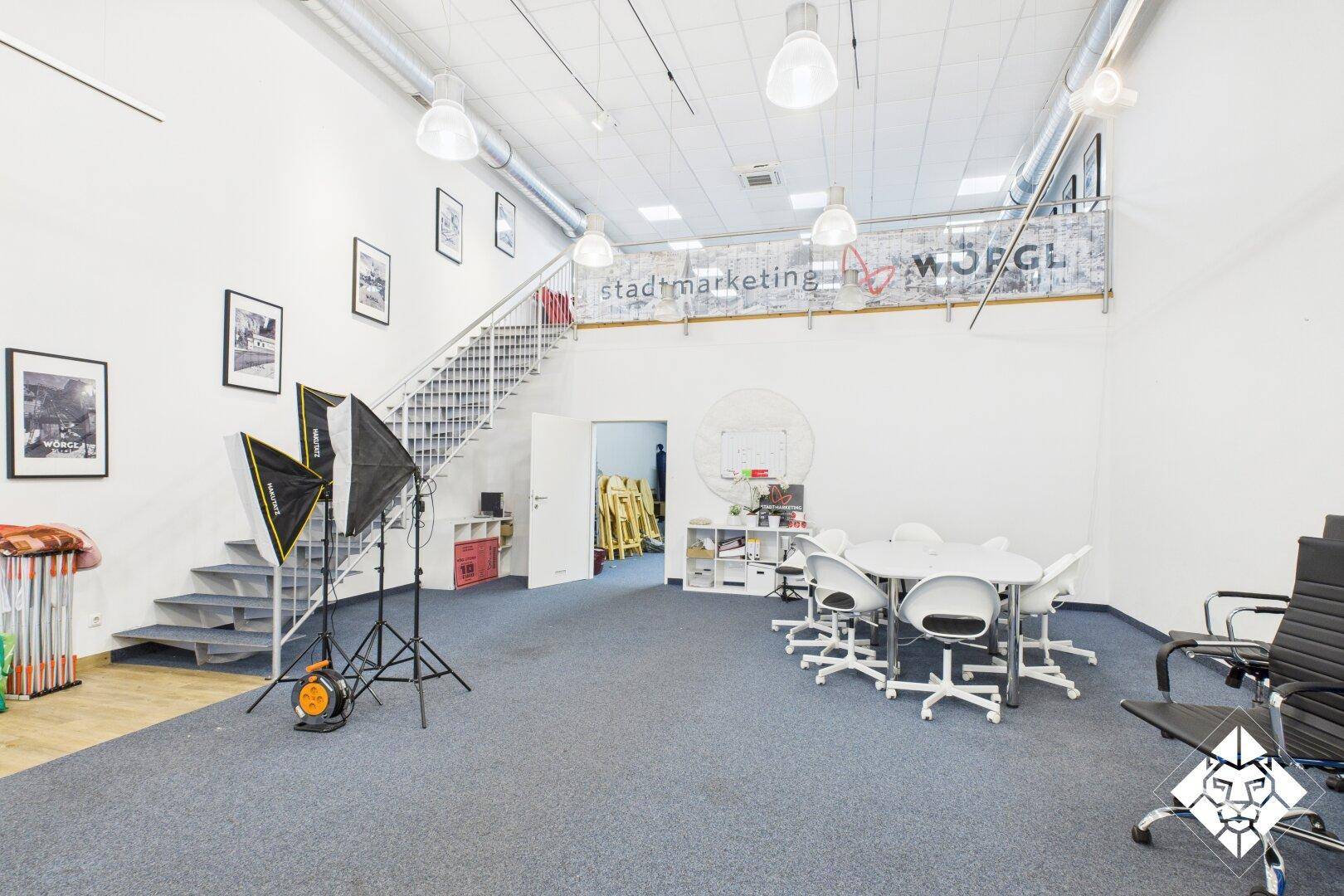 Heller Büroraum mit Treppe, Besprechungsbereich und professioneller Fotoausrüstung.
