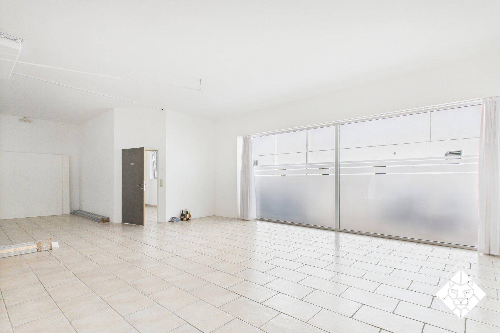 Heller Gewerberaum mit großen, teilweise satinierten Fensterfronten und einer Tür, die zu einem Nebenraum führt.