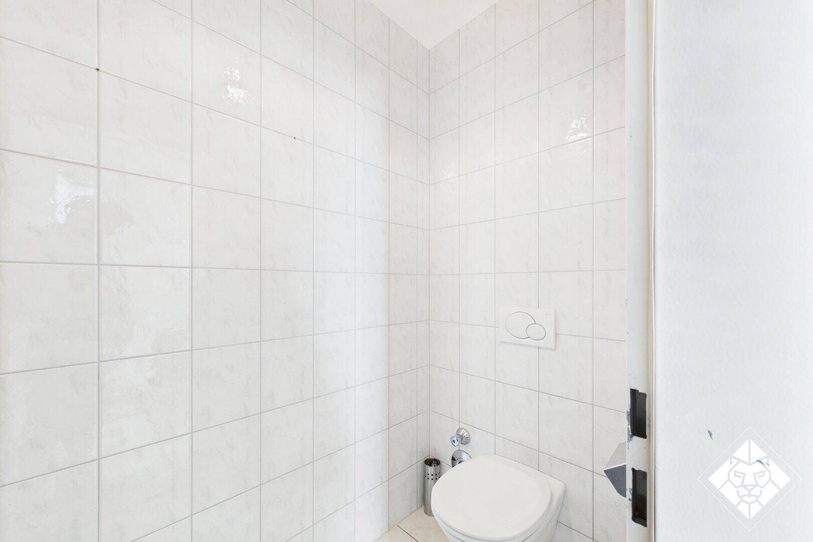 Kleiner Toilettenraum mit weißen Fliesen an den Wänden und einem wandhängenden WC.