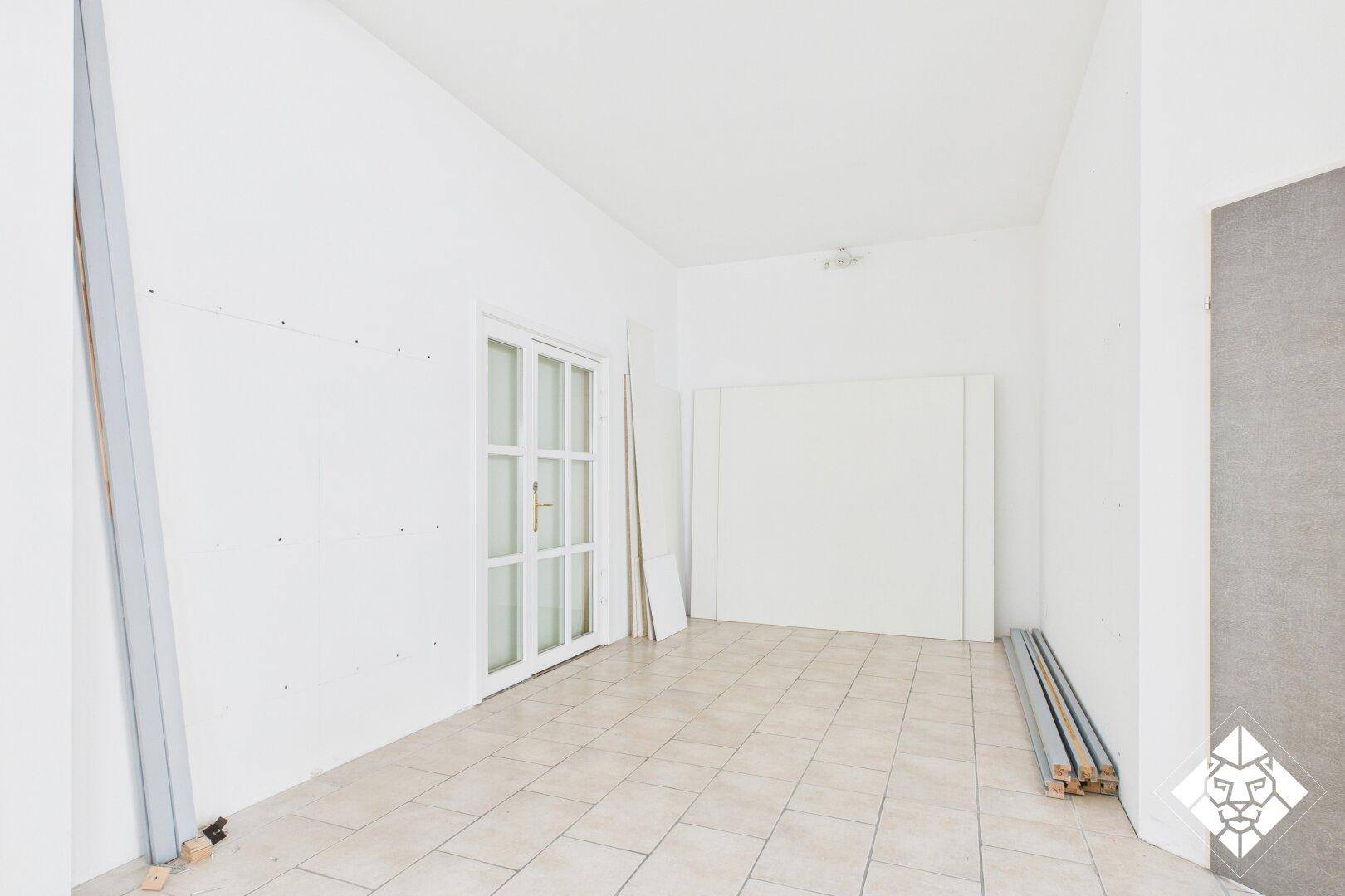 Leerer Raum mit weißen Wänden, Fliesenboden und einer verglasten Tür, bereit für den Innenausbau oder die Einrichtung.