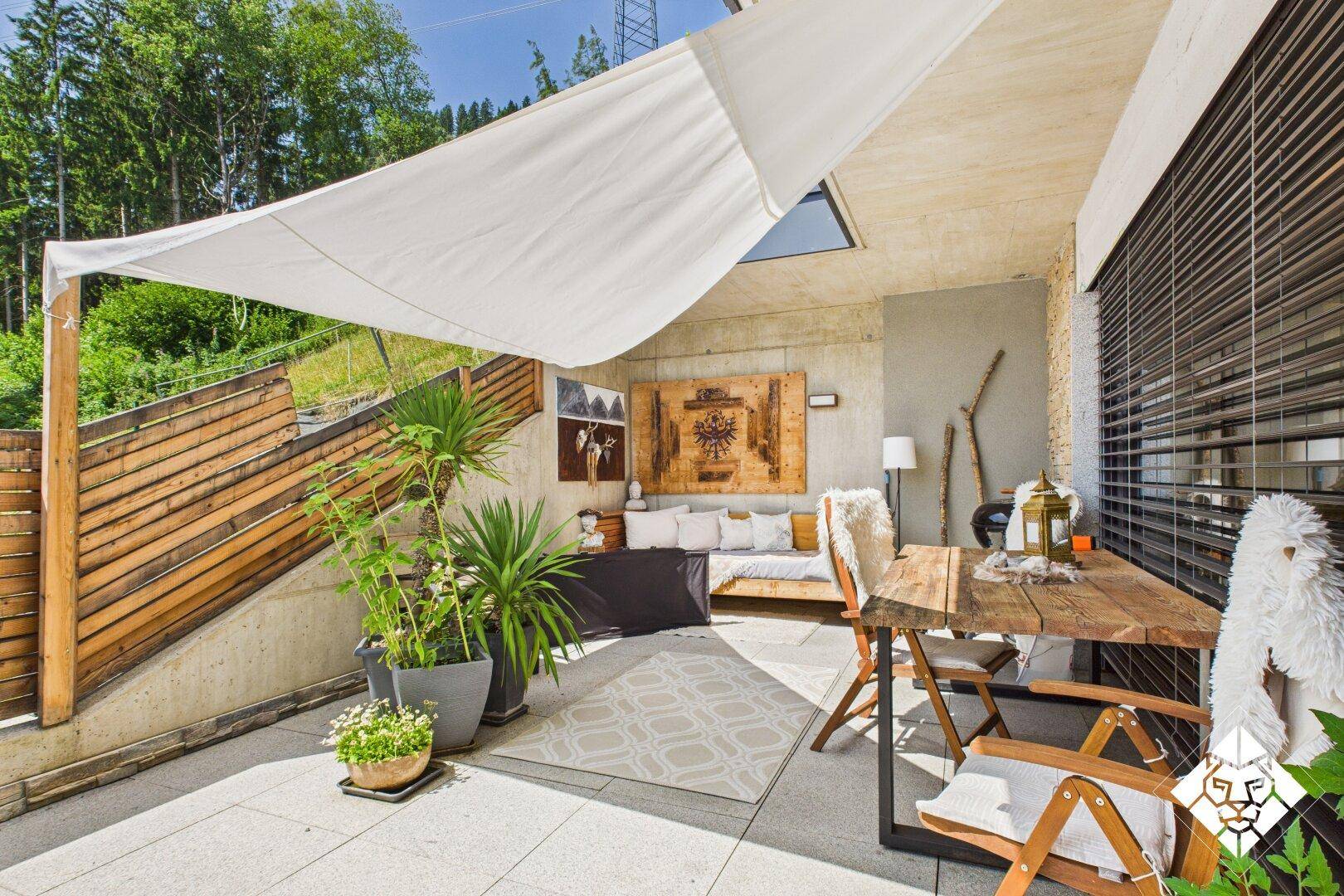 Großzügige Terrasse mit Sonnensegel, Essbereich und Lounge-Möbeln im Grünen.