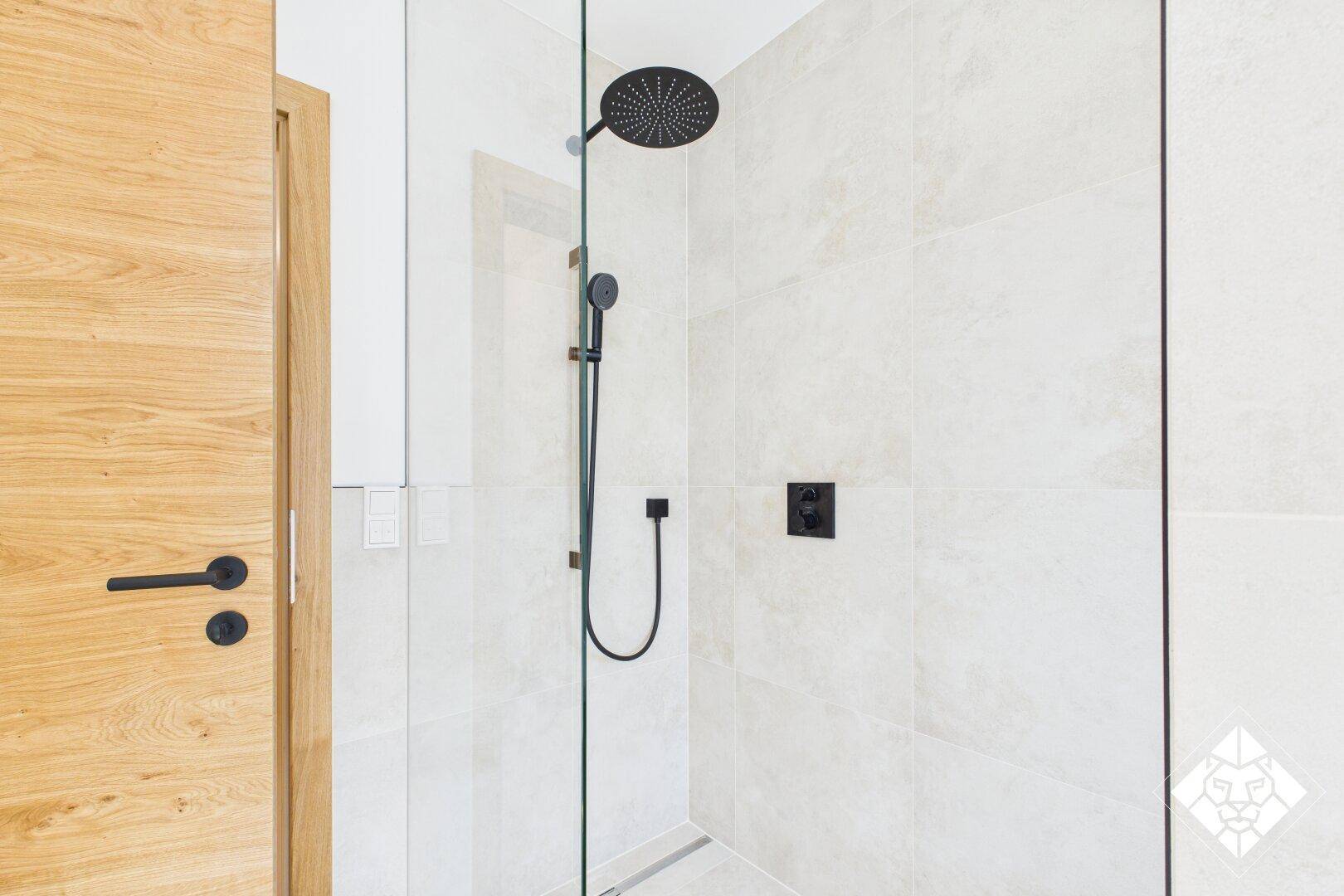 Modernes Badezimmer mit begehbarer Dusche, schwarzen Armaturen und hellen großformatigen Fliesen.